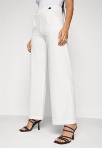 Bílé kalhoty s širokými nohavicemi a vysokým pasem, viditelné kovové knoflíky. V páru s černými páskovými sandály na vysokém podpatku. Hladká textilie.