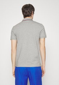 Gray short-sleeve polo shirt with a classic collar, featuring a contrasting dark trim, paired with blue shorts. Simple, clean design.