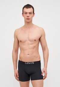 Schwarze Boxershorts mit glatter Textur und elastischem Bund, versehen mit einem grauen Levi's-Logo. Tragen von einem Modell vor neutralem Hintergrund.