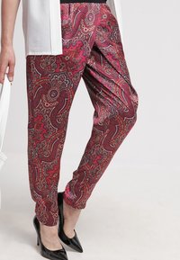 Röda byxor med paisleymönster gjorda av ett mjukt material. Designen har intrikata motiv i rosa, vitt och mörkblåa detaljer.