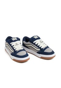 Tumedat sinised suede spordialused, millel on hallid detailid, valged nöörid ja kummist välistald. Omab külglogo ja perforatsioonid parema õhuringluse tagamiseks.