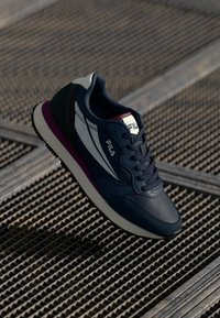 Navy blue sneakers with a leather finish, white accents, and purple midsole. Features lace-up design and Fila logo on the tongue.