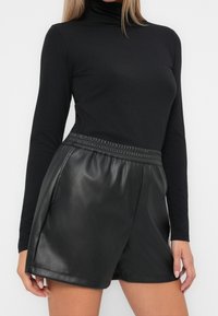 Czarny dopasowany golf w połączeniu z czarnymi, wysokim stanem szortami z imitacji skóry z elastycznym pasem i gładką fakturą.