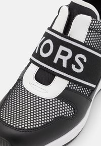 Svartvita träningsskor med mesh-överdel, gummisula, elastiskt band med logotyp och detaljer i syntetiskt läder.