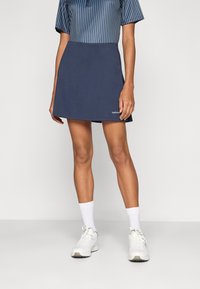 Marineblauwe skort van een gladde stof, met een aansluitende tailleband en een subtiele logo nabij de zoom, gecombineerd met witte sportschoenen en sokken.