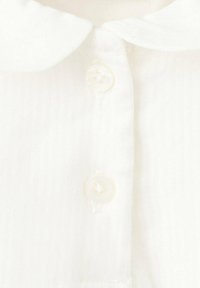 Îmbrăcăminte cu guler alb, realizată dintr-un material texturat. Patru nasturi rotunzi și transparenți sunt vizibili pe fața garniturii.