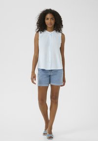 Chemise sans manches bleu clair avec bouton devant, tissu texturé, assortie à un short en denim avec ourlet retroussé et des sandales à glissière bleues.