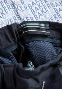 Ciemnoniebieski pas z czarnym guzikiem i pasami. Wewnętrzna podszewka ma wzór w zygzaki. Tło przedstawia jasny wzorzysty materiał.