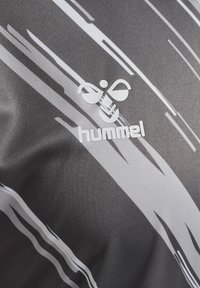 Grå atletisk tröja med vita streckade mönster, med "hummel"-logotypen i vitt i mitten. Tillverkad av mjukt, andningsbart tyg.