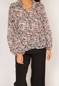 Blouse florale avec un fond noir, ornée de fleurs roses claires et bleues, avec un devant à boutons, des manches longues bouffantes et une coupe décontractée.