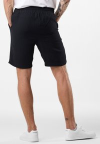 Sorte teksturerede shorts med elastisk talje, der har sidelommer og en afslappet pasform, parret med hvide sneakers.
