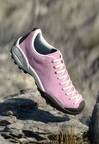 Světlé růžové semišové boty s šedou gumovou podrážkou, kulatou špičkou a bílými tkaničkami. Obsahují texturovanou síťovanou podšívku a logo značky na boku.