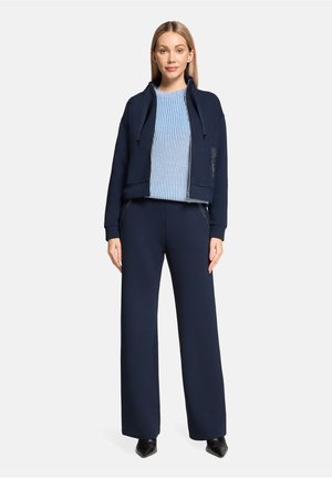 Navy blue zip-up hoodie with hood, paired with a light blue striped sweater and matching pants; smooth fabric, loose fit, and subtle detailing.