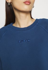 Blaues Sweatshirt mit Rundhalsausschnitt, ausgestattet mit einem gestickten Levi's-Logo in passendem Blau. Glatte Textur und Raglanärmel.