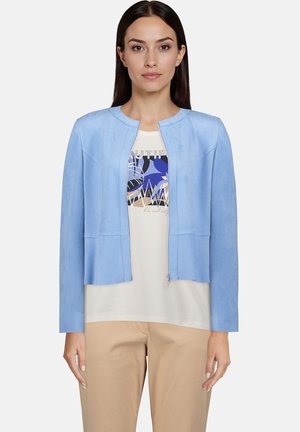 Jasnoniebieska kurtka z faux skóry z okrągłym dekoltem, długimi rękawami, z przodu na zamek błyskawiczny i z dwoma pionowymi detalami szwów. Noszona na koszulce z nadrukiem.