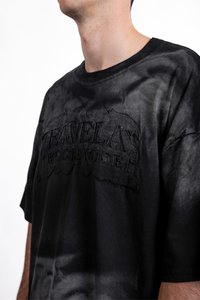 Černé bavlněné tričko s texturovaným, vyšívaným logem "FAVELAS WORLDWIDE". Materiál má nerovnoměrný, vybledlý barevný efekt.