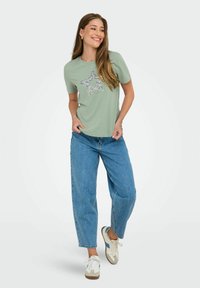 Lys grøn kortærmet T-shirt med et design af en paljettestjerne, parret med højtaljede blå jeans og afslappede sneakers.