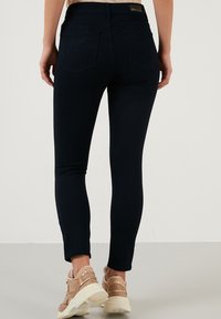 Jeans ajustados en denim azul oscuro con una textura suave, diseño de cinco bolsillos y detalles de costura visibles. Combínalos con zapatillas de colores claros.