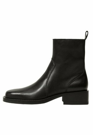 Bottine en cuir noir avec talon carré bas, bout arrondi, détails de couture latéraux et languette à l'arrière.