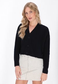Cardigan cropped blu navy in maglia a coste con scollatura a V, caratterizzato da tre grandi bottoni e maniche lunghe, abbinato a una gonna a righe.