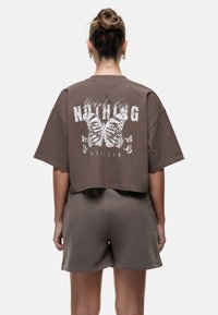 T-shirt corto marrone con una grafica di farfalle bianche e testo sul retro. Abbinato a pantaloni corti marroni coordinati. Tessuto morbido, vestibilità comoda.