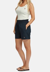 Laivastonsiniset shortsit, joissa on joustava vyötärönauha ja sivutaskut; yhdistetty valkoiseen, ribbineulottuun topiin, jossa on pieni kirjailtu logo.