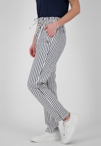 Pruhované kalhoty v námořnické modři a bílé s elastickým pasem, šňůrkou na stažení a bočními kapsami. Textura se zdá být hladká; kombinujte s bílými teniskami.