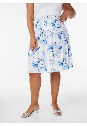 Woman wearing knee-length white skirt with blue floral print, white sleeveless top, and light blue strappy heeled sandals.