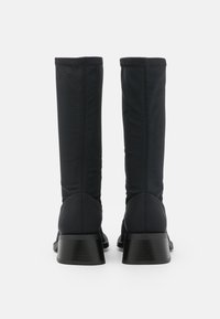 Svarta knähöga stövlar i ett mjukt, stretchigt material, med en tjock geometrisk klack och sömlös sömnad längs baksidan.