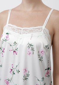 Camiseta de satén blanca con estampado floral en tonos rosas, con un delicado ribete de encaje en el escote y tirantes delgados ajustables. Textura suave.