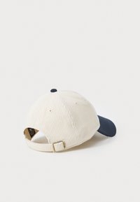 Camelkleurige corduroy pet met een marineblauwe klep, met een gestructureerd oppervlak en een verstelbare band aan de achterkant.