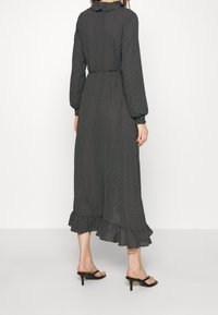 Svart maxiklänning med vita prickar, långa ärmar, volangdetaljer vid ärmsluten och fållen. Har en figursydd midja och en utsvängd kjol. Slät tygtextur.