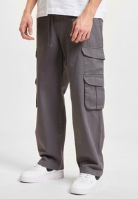 Gray cargo pants with multiple side pockets, made from soft fabric, featuring a drawstring waist and relaxed fit, paired with white sneakers.