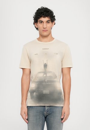Beige bomulds t-shirt med et falmet grafik af en kvinde på en bil, med teksten "DON DUP MADE IN ITALY" trykt ovenfor. Kortærmet og med rund hals.