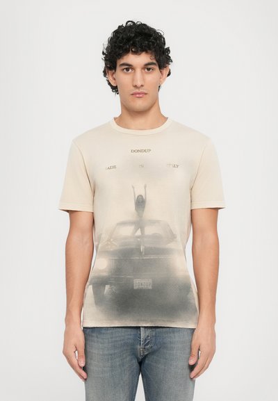 T-shirt en coton beige avec un graphisme vieilli représentant une femme sur une voiture, avec "DON DUP MADE IN ITALY" imprimé au-dessus. Manches courtes et col rond.
