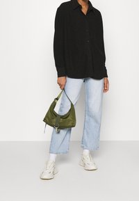 Chemise noire à boutons, à manches longues, jean droit en denim bleu clair et sac en satin olive avec un détail de crochet et de sangle.