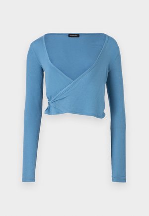 Lyseblå cropped langærmet top med v-hals og omslagdesign, lavet af ribbet stof. Har en drapering ved taljen.