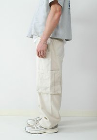 Beige cargo broek met zijzakken, rechte pijpen, van katoen met versterkte stiksels, in combinatie met grijze en witte sneakers.