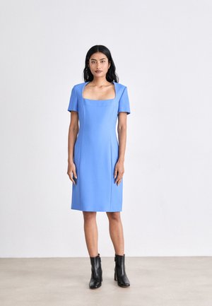 Blue square-neck dress with short sleeves, smooth fabric, fitted silhouette, knee-length, worn with black ankle boots. Minimalist design.