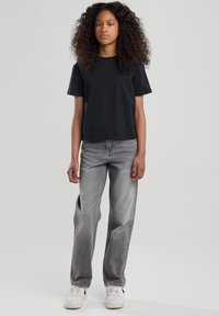 Camiseta de algodón negra con mangas cortas, combinada con unos vaqueros de mezclilla grises de cintura alta y zapatillas blancas con detalles en negro.