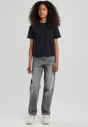 T-shirt en coton noir à manches courtes, associé à un jean en denim gris taille haute et des baskets blanches avec des accents noirs.