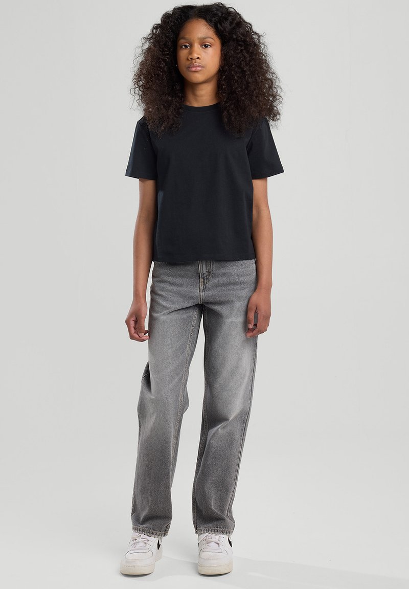 Camiseta de algodón negra con mangas cortas, combinada con unos vaqueros de mezclilla grises de cintura alta y zapatillas blancas con detalles en negro.