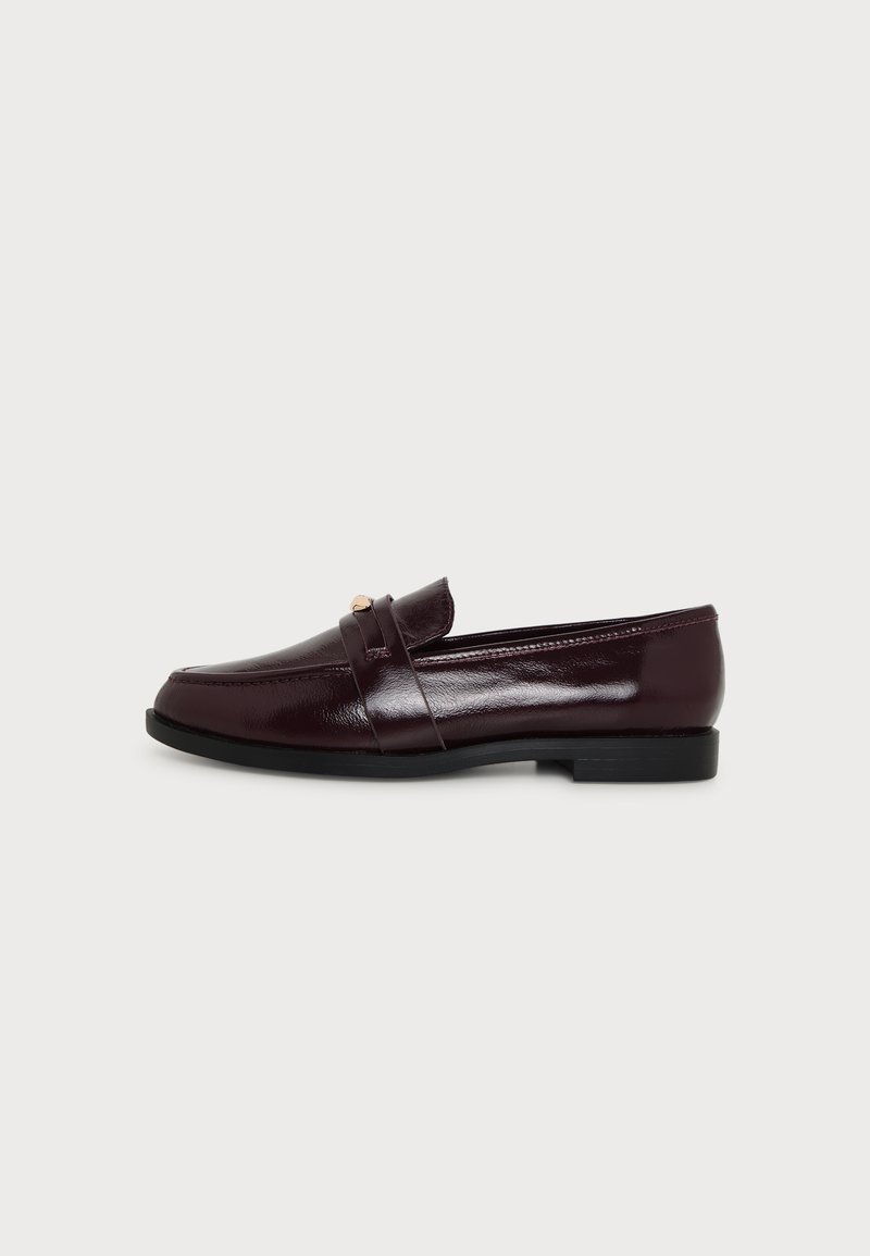 Mocassin en cuir marron foncé avec un petit détail métallique doré sur la bride et une semelle plate noire, vu de côté.