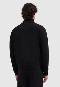Zwarte sweatshirt met een hoge kraag, ribbels aan de mouwen en onderkant, gemaakt van zachte stof, met een eenvoudig ontwerp zonder zichtbare logo's of patronen.