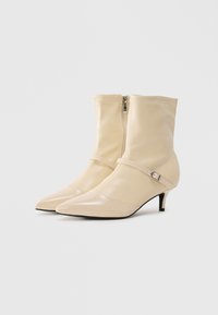 Beige pointed-toe ankle boots with low heels, side zipper, and thin strap with a small silver buckle on a white background.