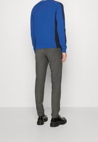Maglione blu con pannelli laterali neri, caratterizzato da tre strisce nere sulle maniche. Pantaloni grigi su misura con una trama liscia. Scarpe nere.