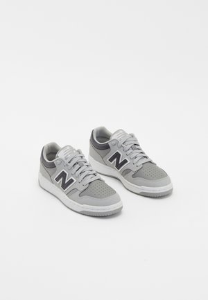 Coppia di sneaker New Balance grigie con suole e lacci bianchi, area della punta perforata e logo nero "N" sui lati.