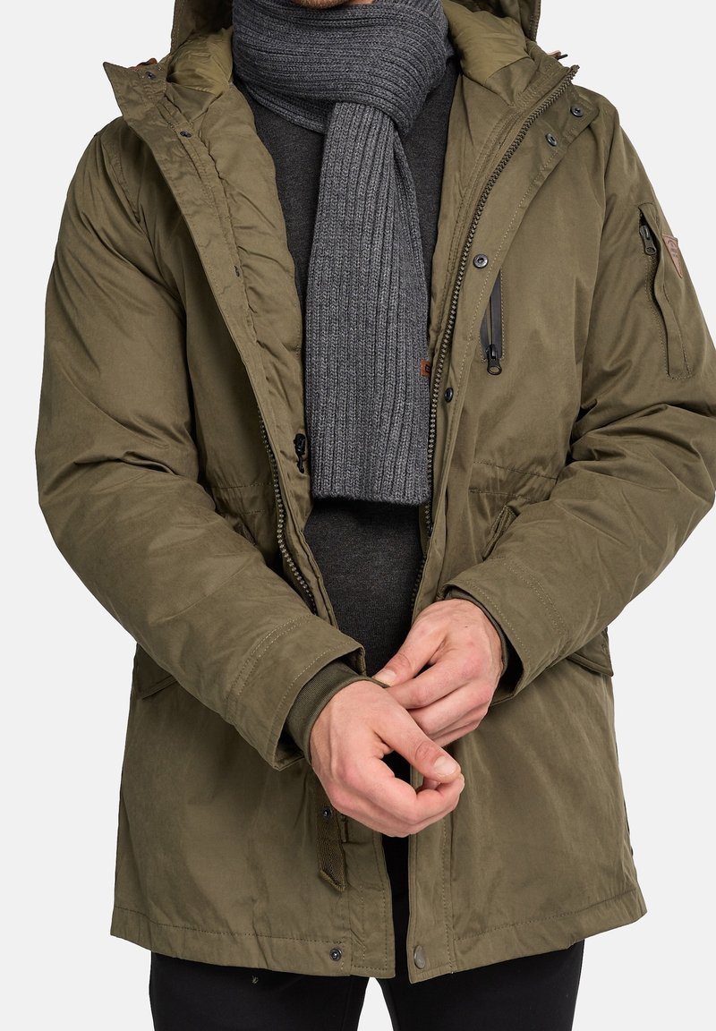 Olivgrüner isolierter Parka mit Kapuze, Reißverschluss und Druckknopfverschlüssen sowie einem gerippten grauen Schal. Strukturiertes Material mit Seitentaschen.