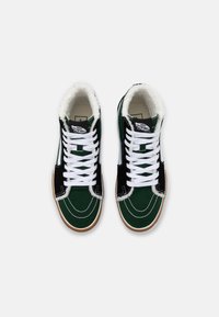 Vysoké tenisky s zeleno-černým designem, vyznačující se bílými tkaničkami, kožešinovým podšívkou a tan gumovými podrážkami. Jasné švy a detaily loga.