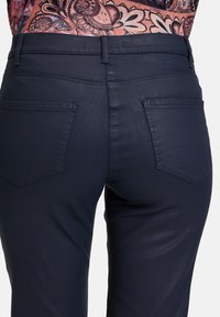 Dunkelblaue, hoch geschnittene Hose aus Stretchstoff, mit zwei Rückentaschen mit gesticktem Design. Glatte Textur und schlanker Schnitt.